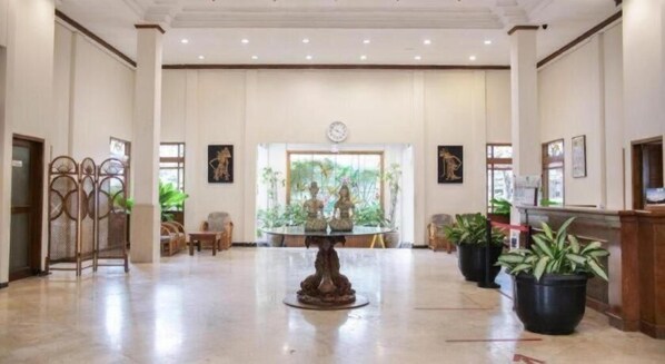 Eine geräumige Lobby mit einem runden Tisch in der Mitte, Zimmerpflanzen und gerahmten Kunstwerken an den Wänden.