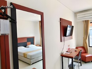 Ein Hotelzimmer mit einem Bett, einem Schreibtisch mit Stuhl, einem Fernseher und einem Fenster mit Vorhängen.