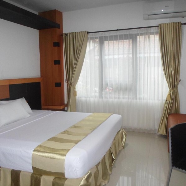 A hotel room with a bed, a chair, a wooden headboard, and an air conditioning unit.