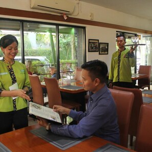 Un interior de restaurante con mesas, sillas y un camarero atendiendo a un cliente.