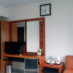 Une chambre d’hôtel avec un bureau en bois, une télévision, une chaise, une machine à café et une horloge murale.