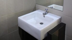 Un baño con lavamanos blanco, espejo y paredes con azulejos.