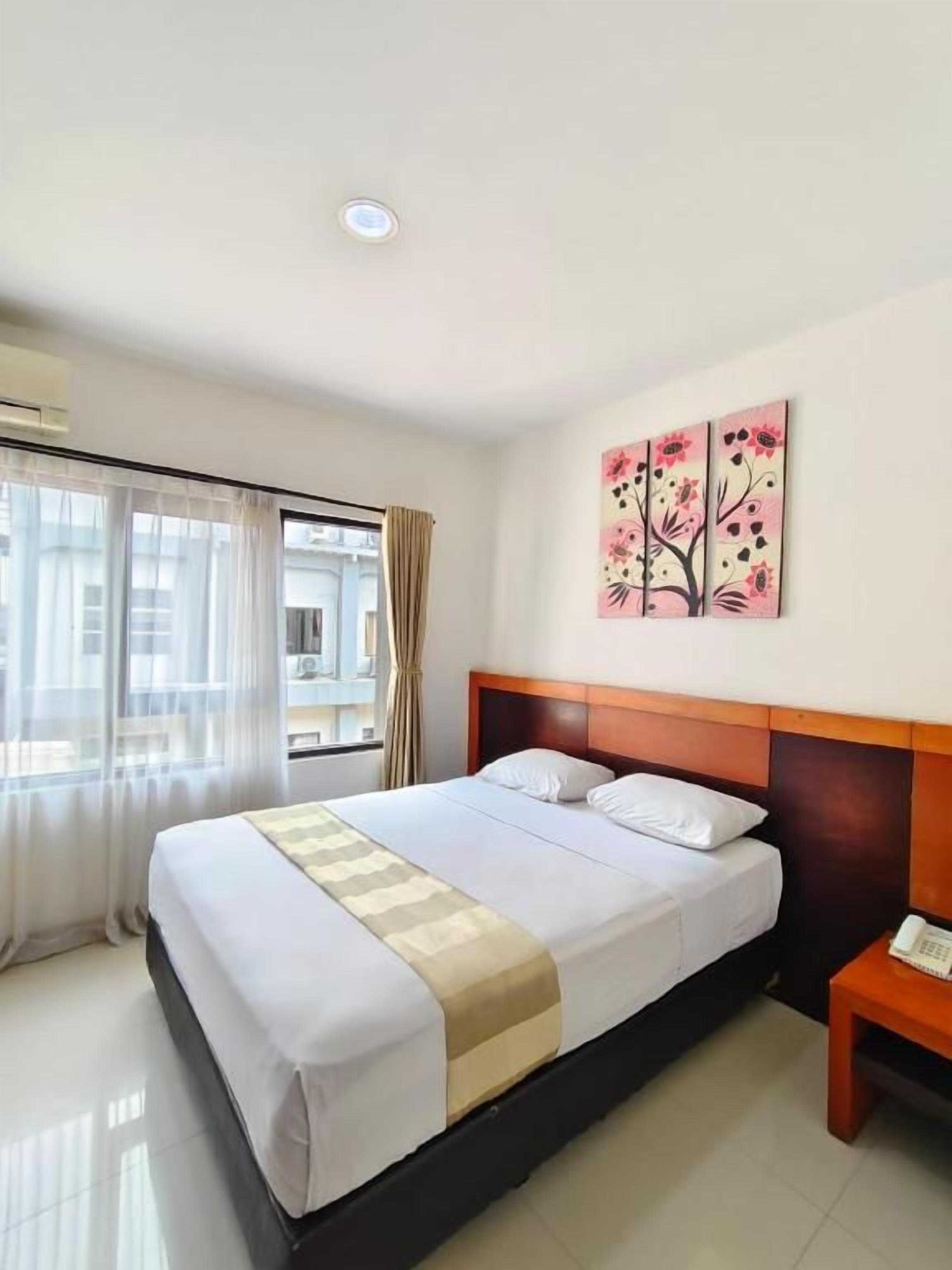 A hotel room with a bed, a bedside table with a phone, and a window with curtains.