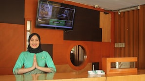 A hotel reception desk with a television mounted above it displaying a menu. - Hotel Grand Karawang Indah (Karawang)