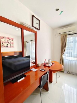 Habitación de hotel con televisión, escritorio, silla, espejo, reloj y ventana con cortinas.