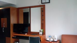 A hotel room with a wooden desk, a television, a large mirror, a sofa, and a clock on the wall. - Hotel Grand Karawang Indah (Karawang)