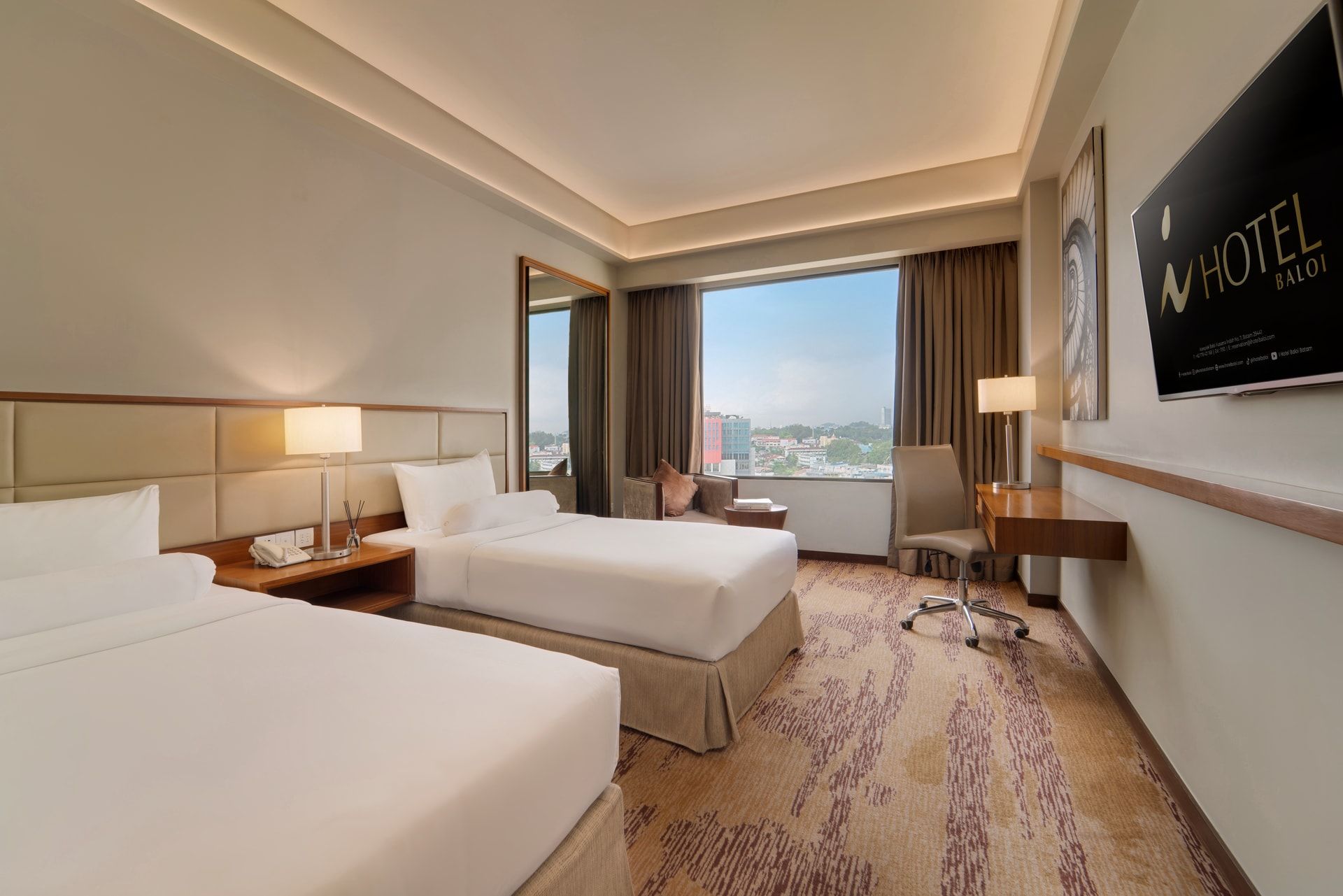 Ein Hotelzimmer mit zwei Betten, einem Schreibtisch, einem Stuhl und einem großen Fenster mit Blick auf die Stadt.