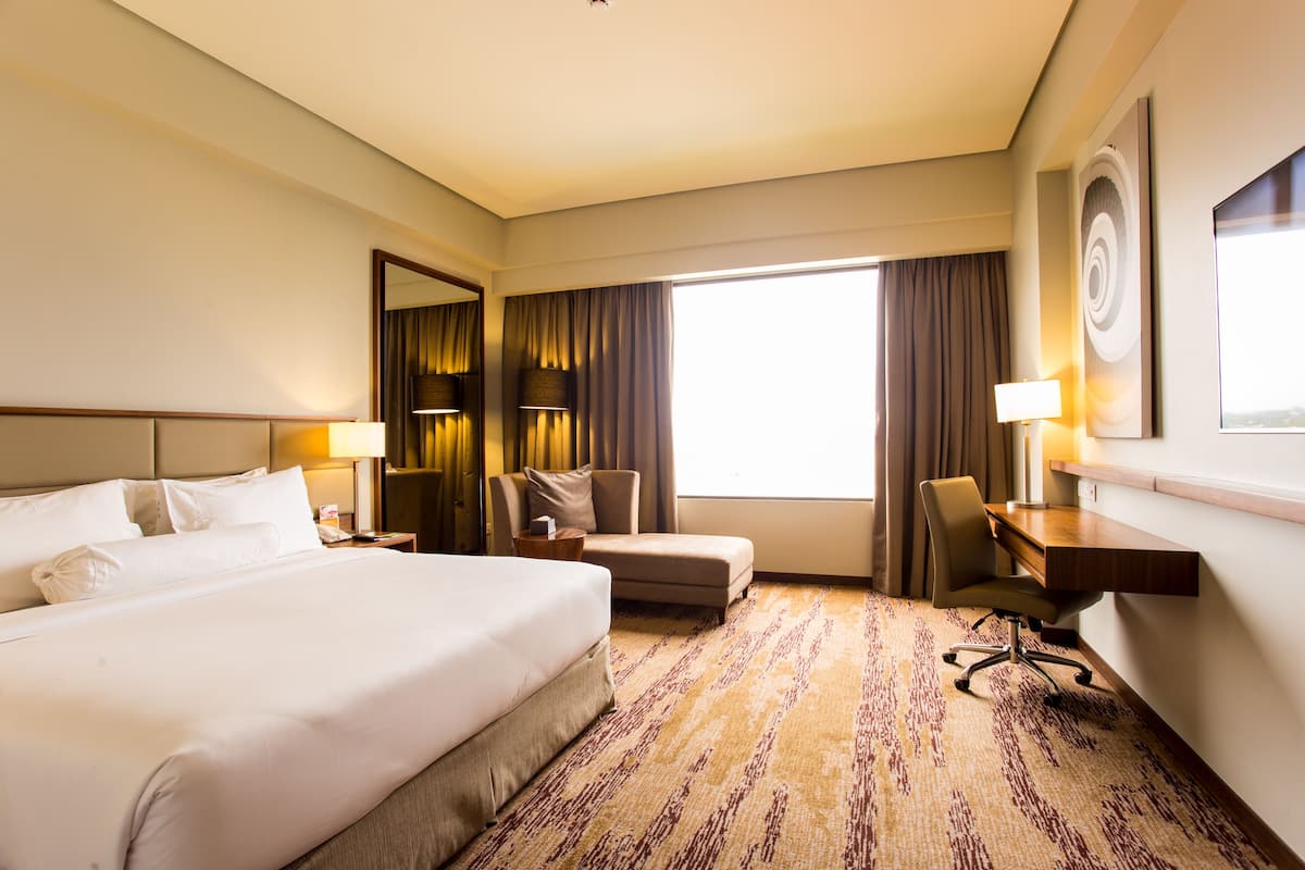 A hotel room with a large bed, a desk, a chair, and a window with curtains.