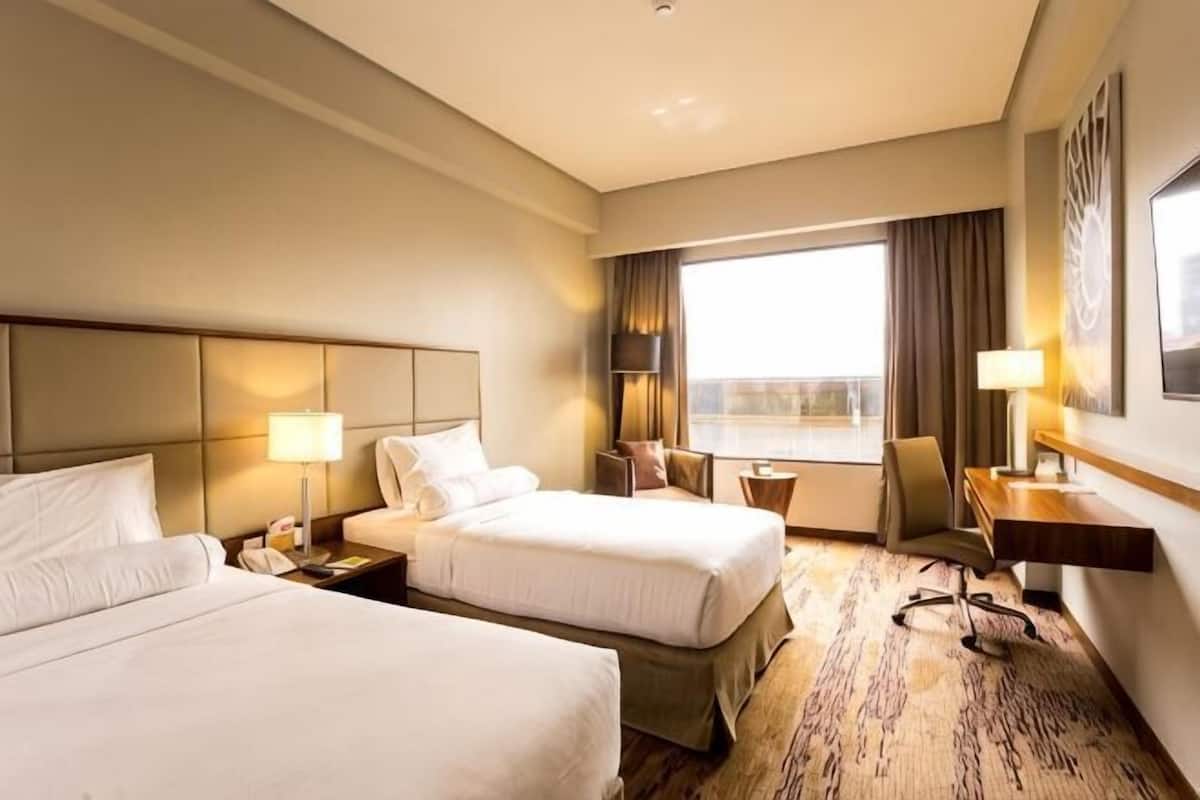 A hotel room with two beds, a desk, a chair, and a large window.