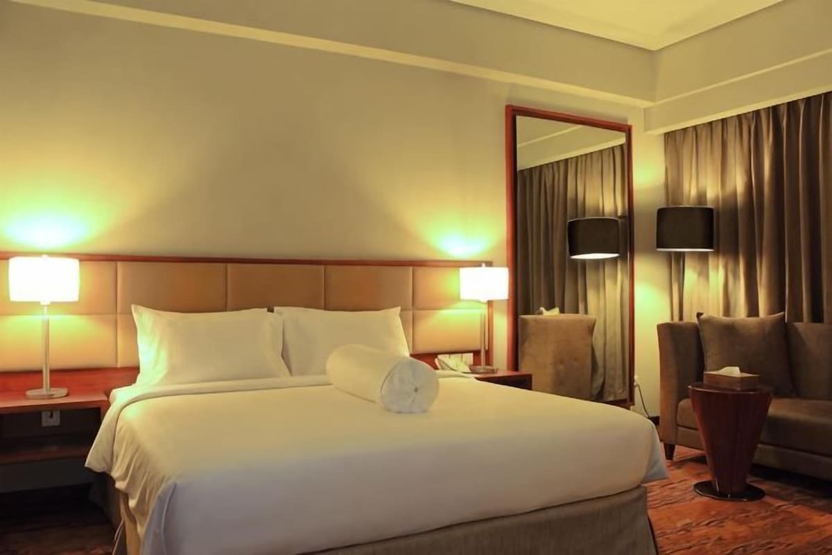 A hotel room with a large bed, two bedside lamps, a TV, a sofa, and a mirror.