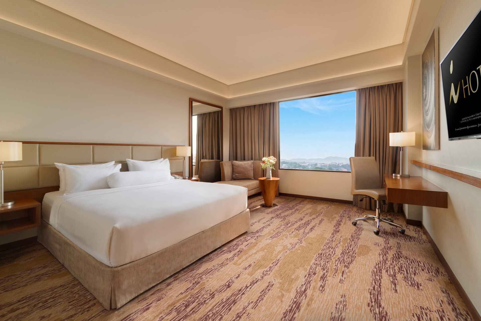 A hotel room with a large bed, a desk, a chair, and a view of the city.