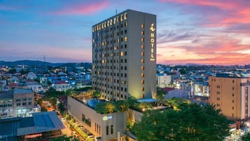 A high-rise hotel with multiple floors, surrounded by urban buildings, and a clear sky at dusk.