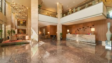A spacious lobby with a marble reception desk, seating areas, and a mezzanine level with glass railings.