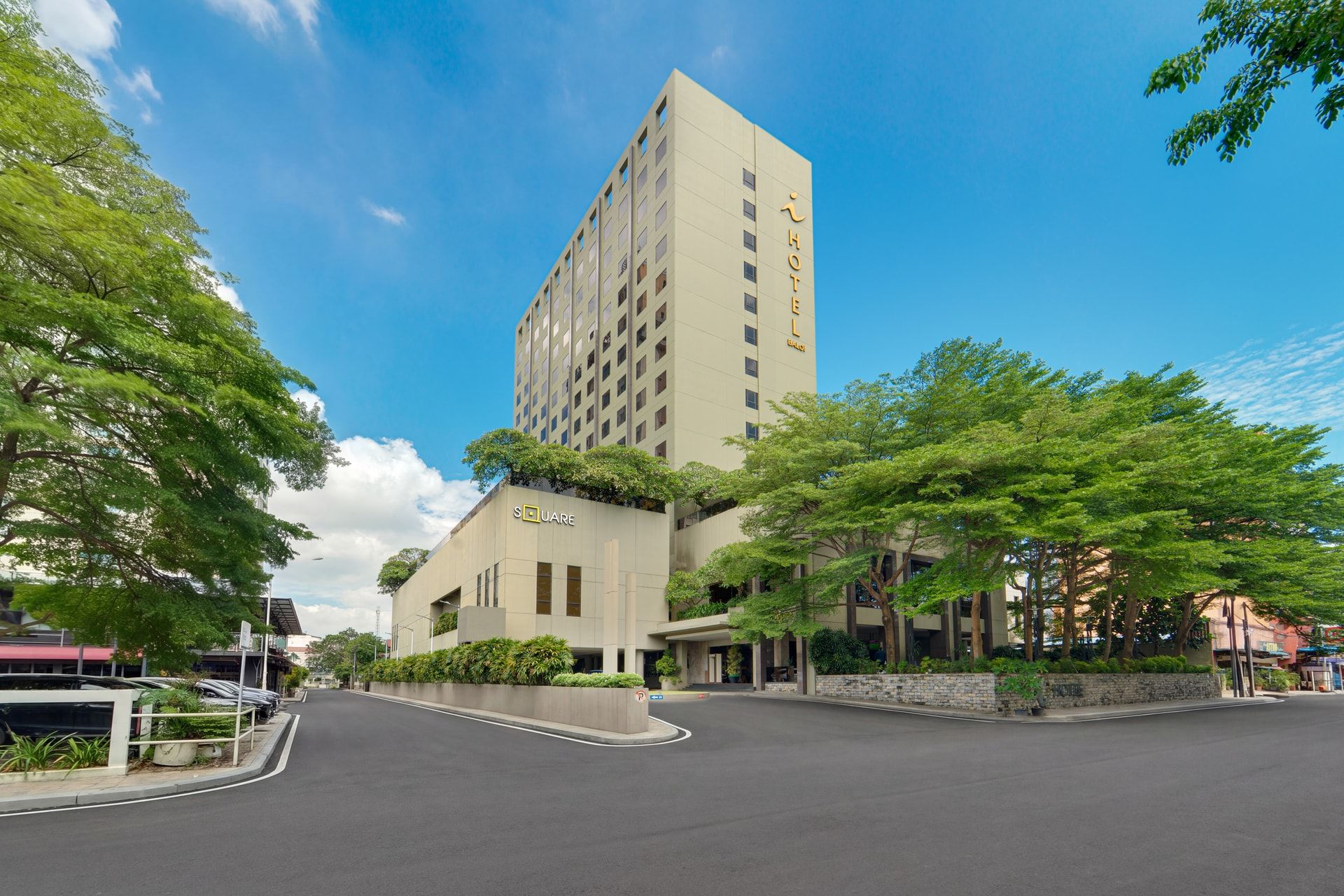 A modern hotel with a prominent tower, a ground-level building with a sign, and a street in front.