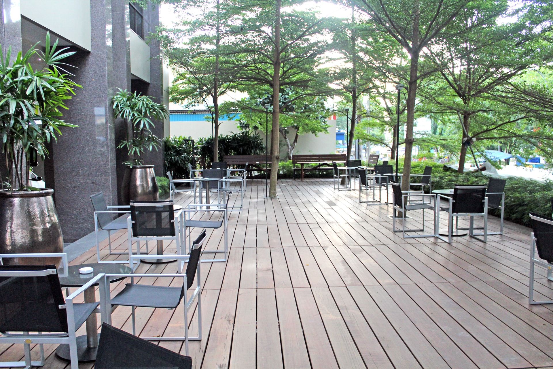 An outdoor seating area with tables and chairs, surrounded by trees and potted plants.