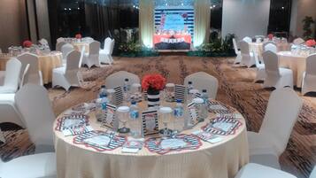 A banquet hall with round tables set for a formal event, featuring name cards, water bottles, and glassware.