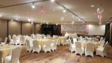 Un salón de banquetes con mesas redondas, sillas blancas y piso alfombrado.