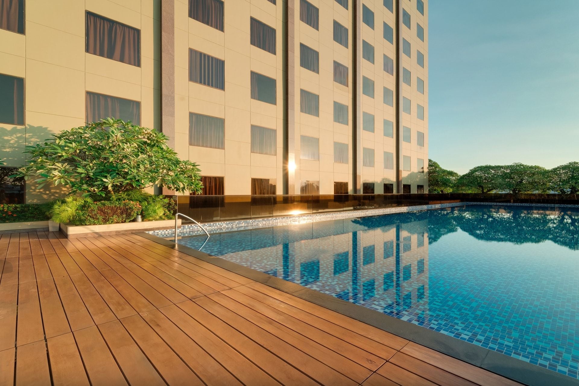 A modern hotel with a swimming pool, wooden deck, and lush greenery.