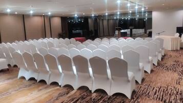 A conference room with rows of white chairs, a stage with a podium, and a carpeted floor.