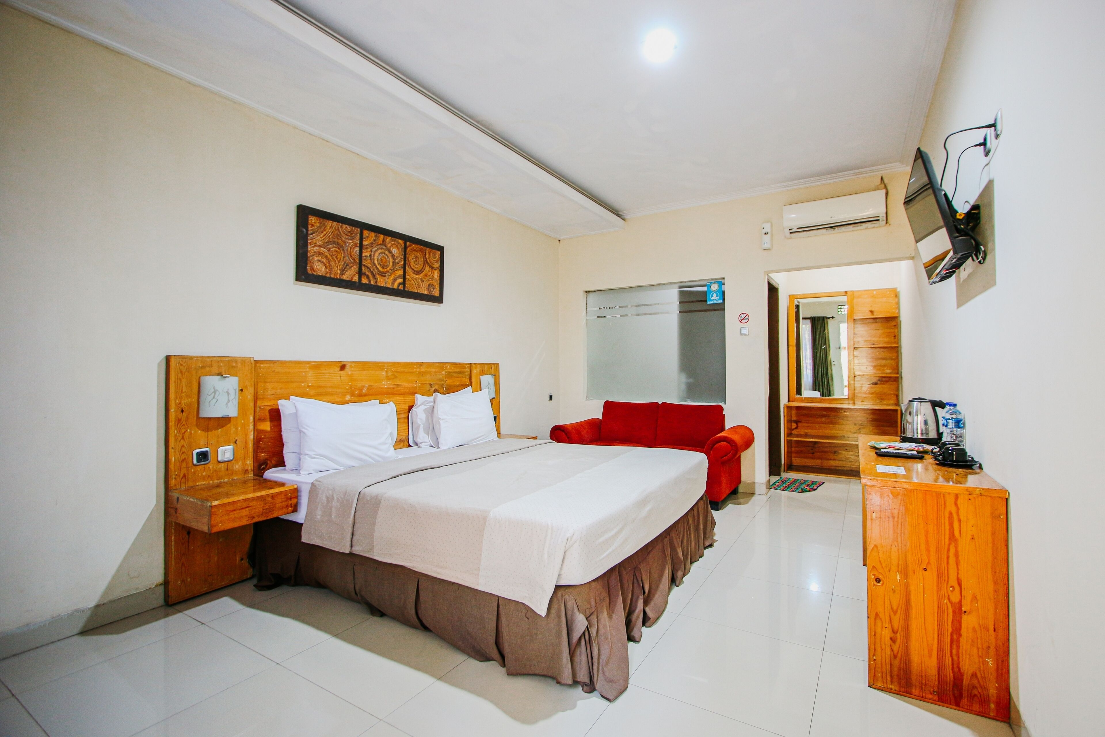 A hotel room with a wooden bed, a red chair, a wooden desk, and a television mounted on the wall.