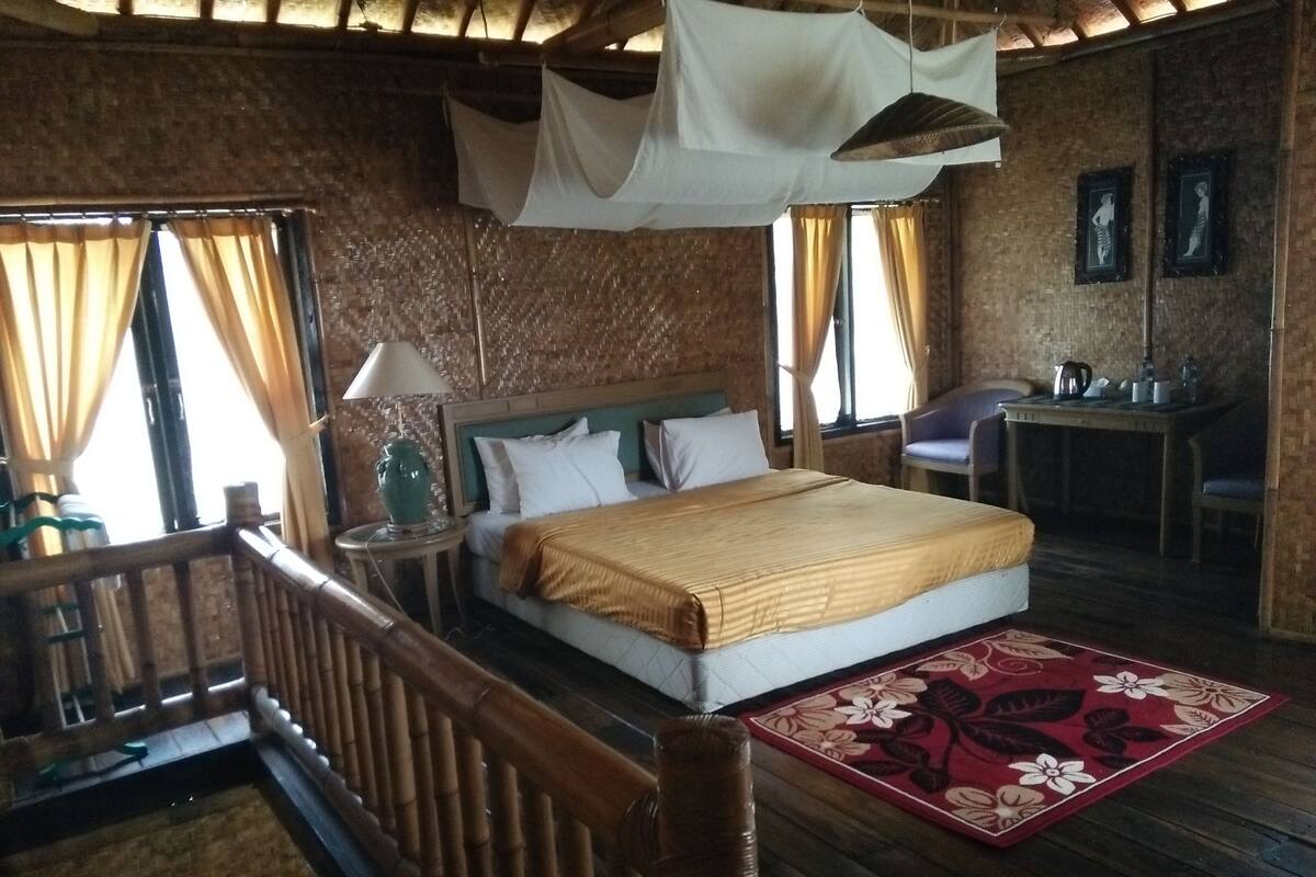 Quarto com cama, mesa de cabeceira, luminária e tapete floral vermelho.