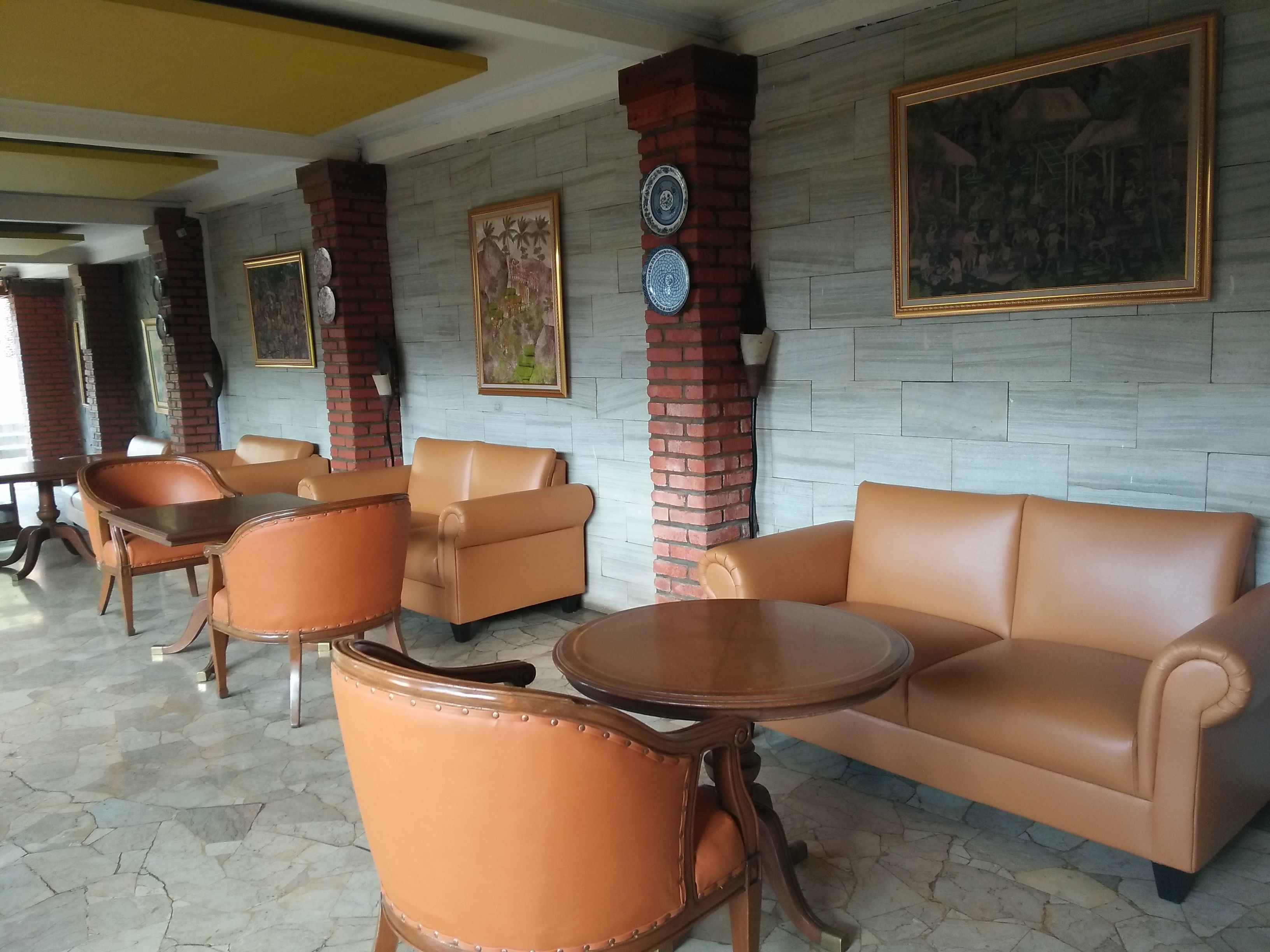 A lobby with leather sofas and armchairs, a brick column, and a tiled floor.