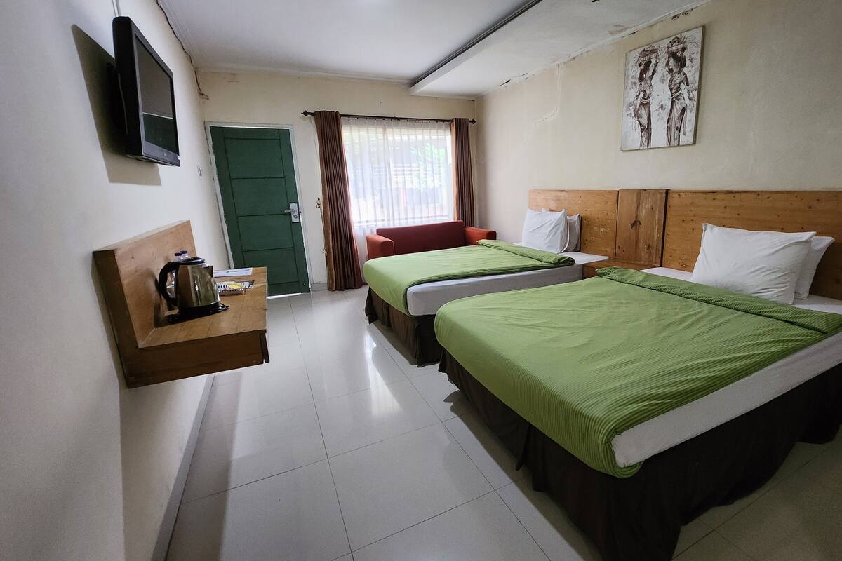 Quarto de hotel com duas camas, uma secretária com um bule, uma televisão e uma porta.