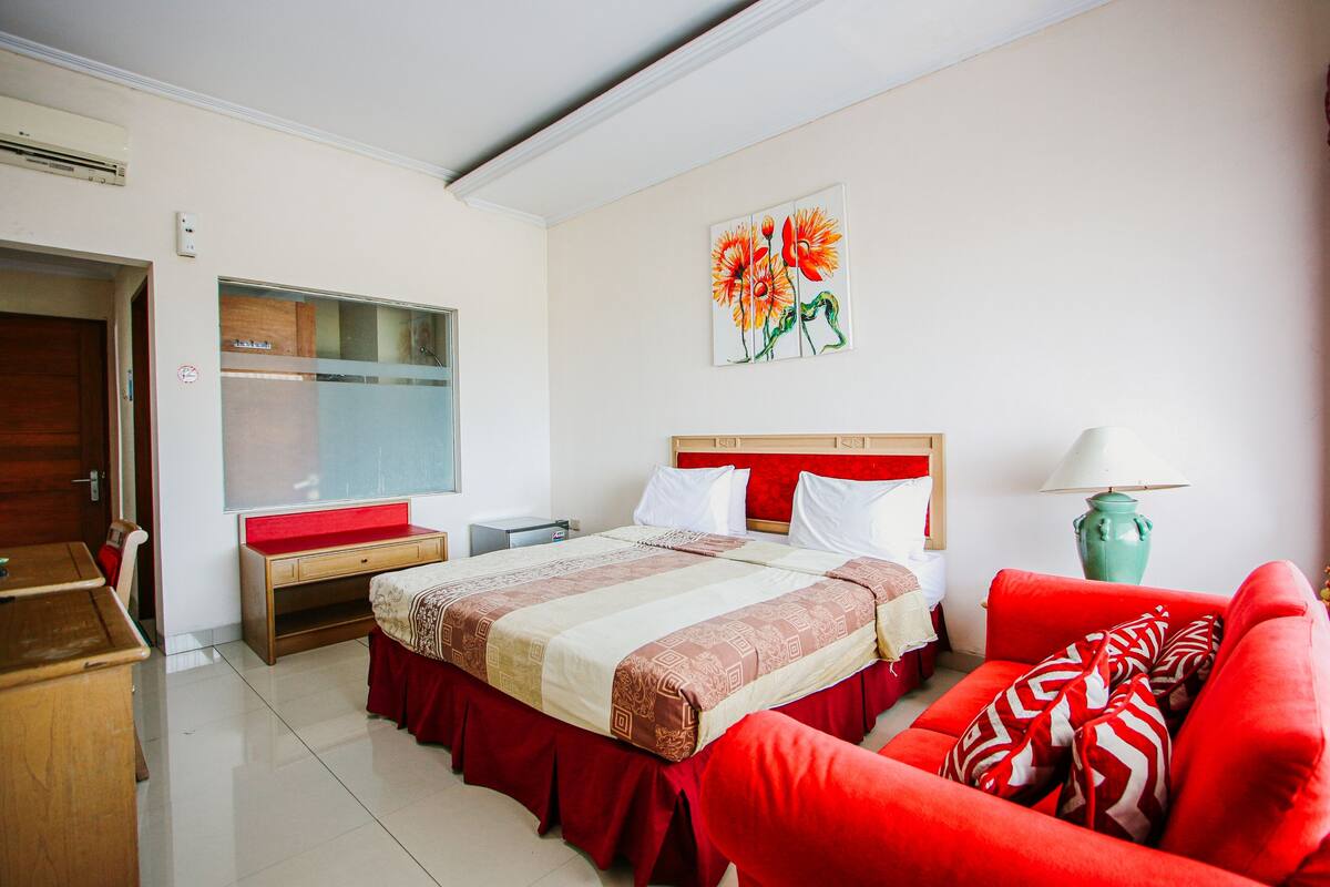 Quarto de hotel com cama, sofá vermelho, escrivaninha e um quadro na parede.