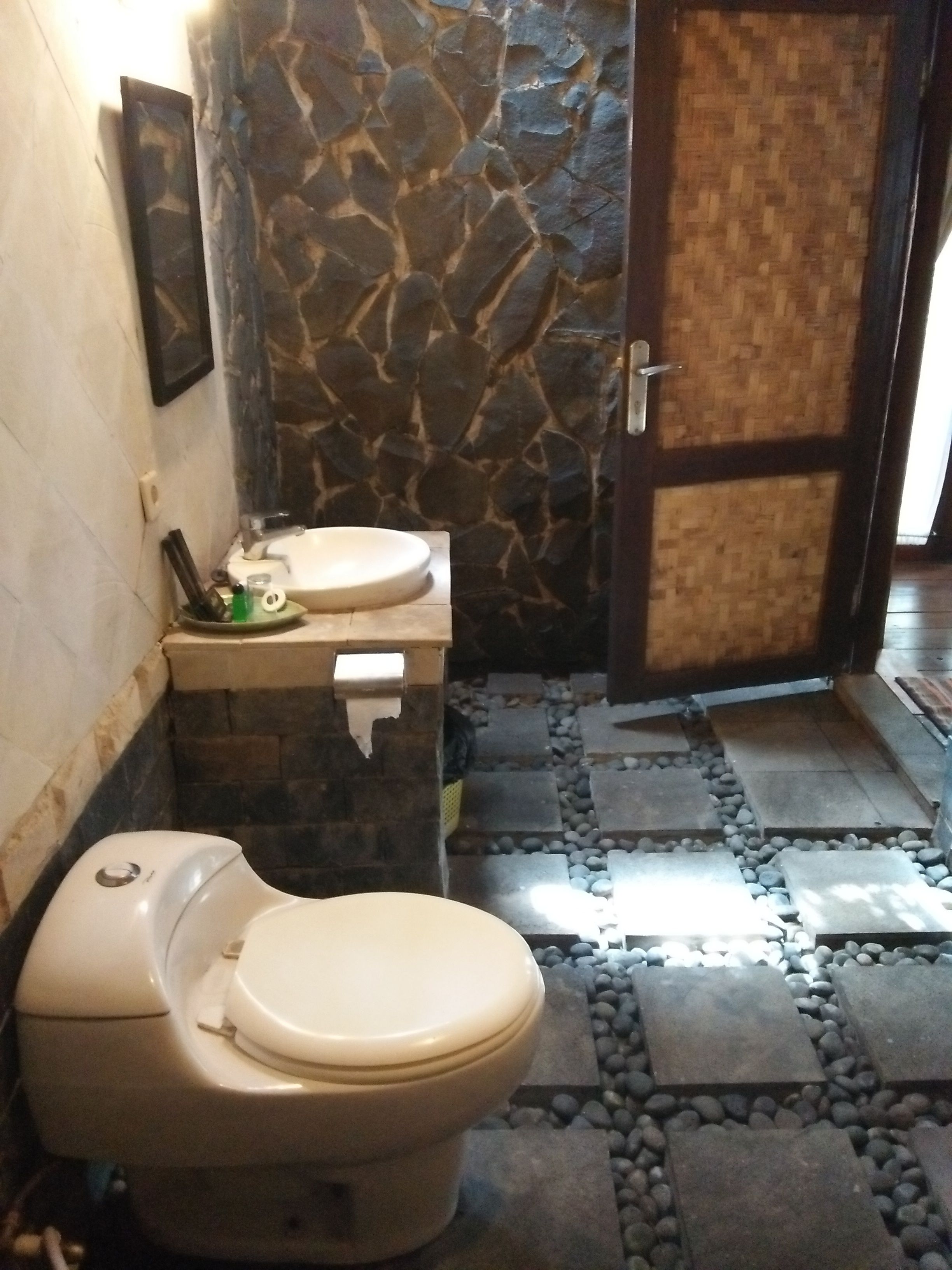 A bathroom with a toilet, sink, and stone wall.