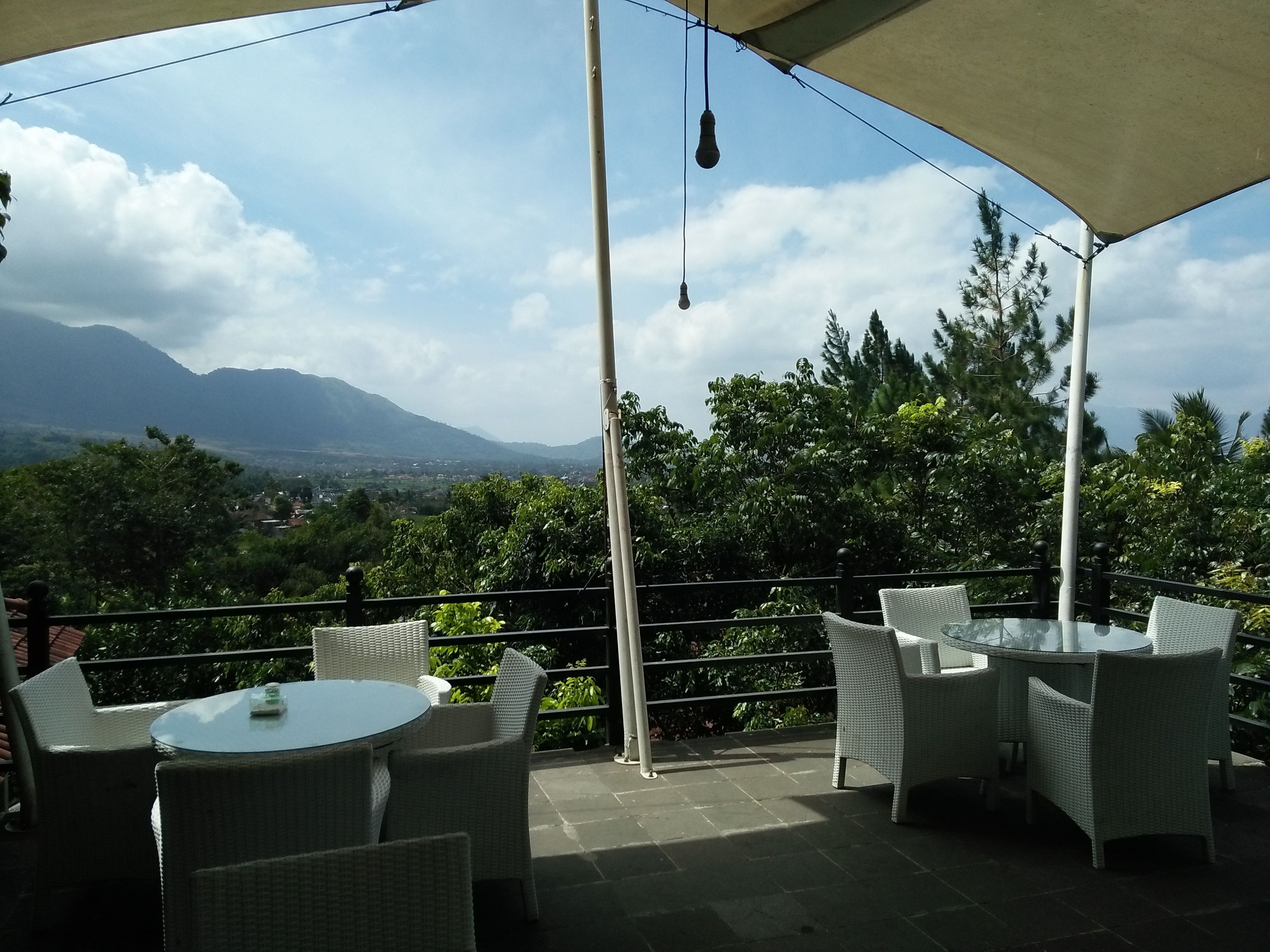 An outdoor patio with wicker furniture and a glass table, overlooking a mountainous landscape.
