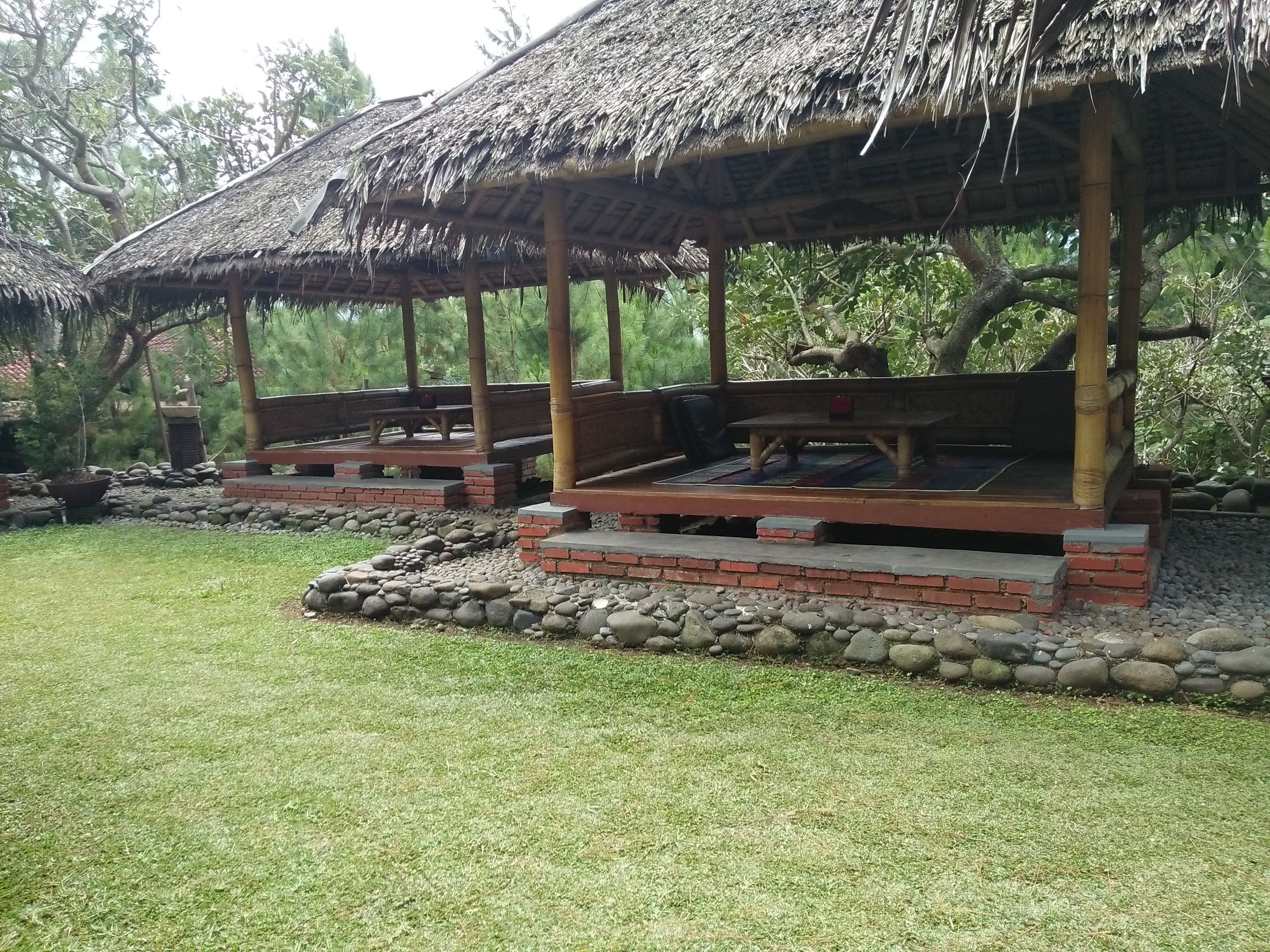 A thatched-roof pavilion with wooden benches and a stone pathway.