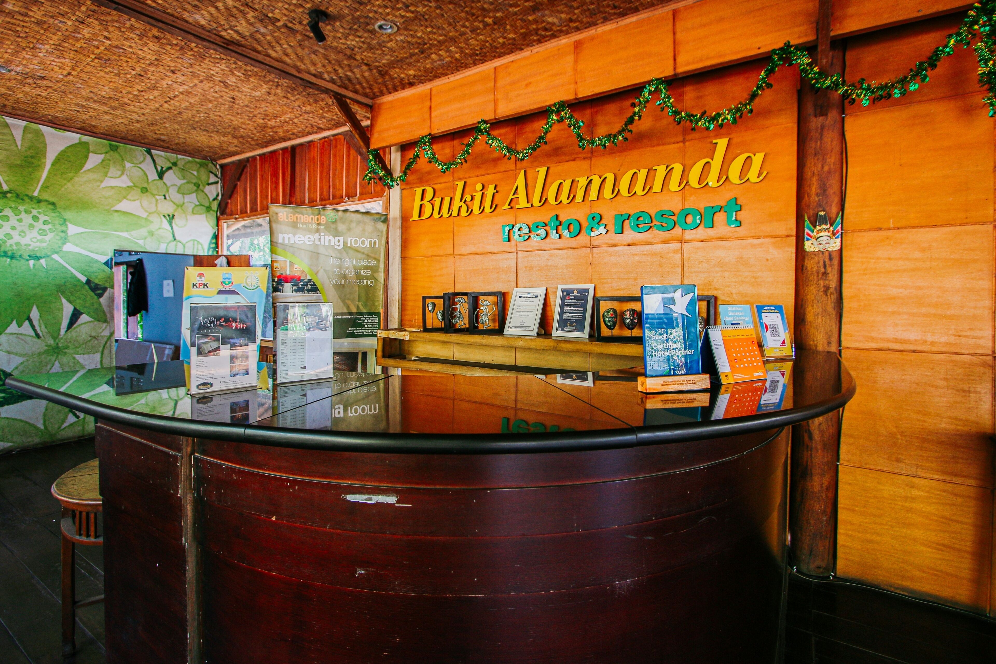 A reception desk at Bukit Alamanda resort with a wooden interior, a glass counter, and a wall with a 'meeting room' sign.