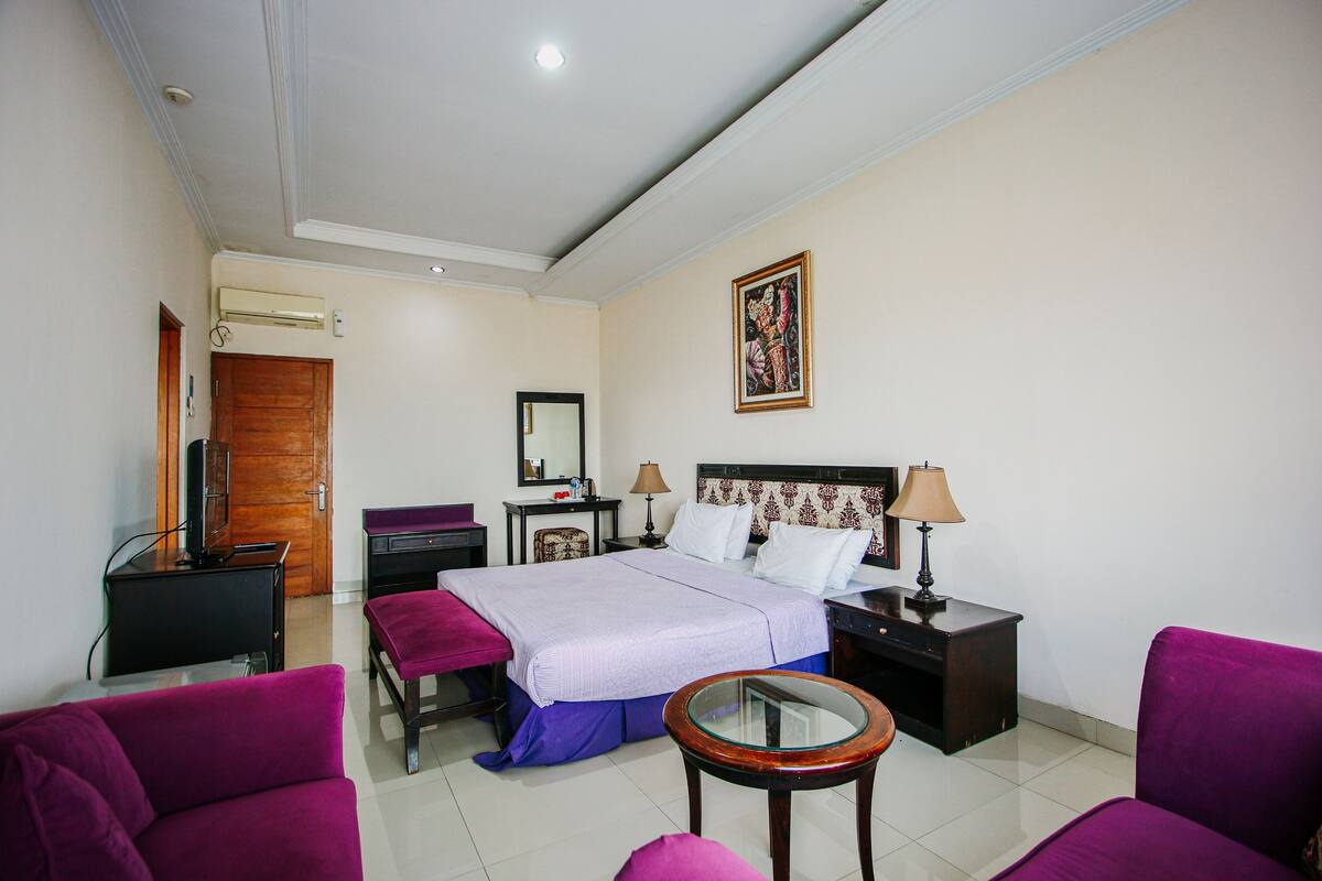 Quarto de hotel com cama, escrivaninha, cadeira, mesa redonda e televisão.
