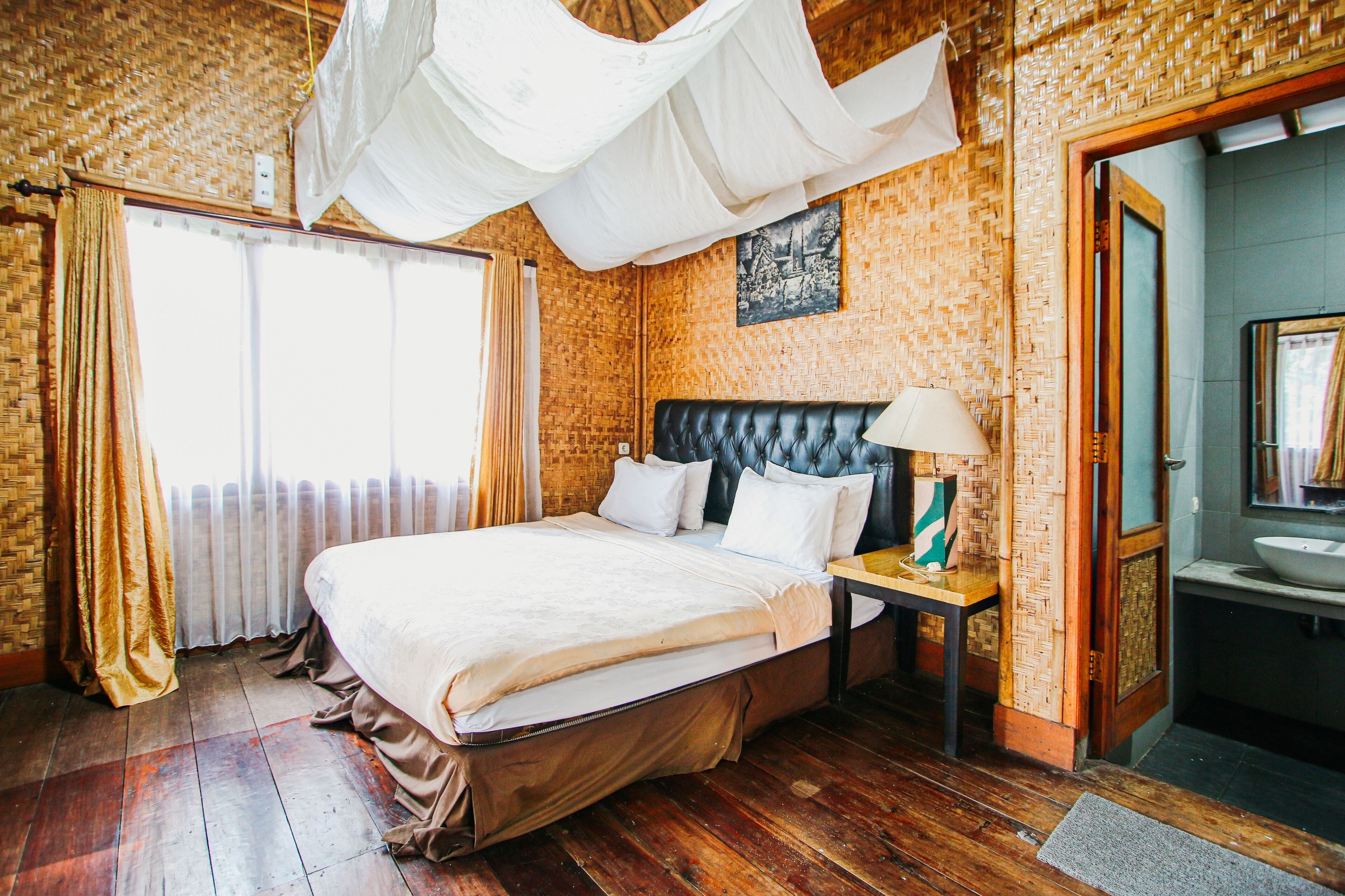 Una habitación con una cama grande, una mesita de noche, una lámpara y un baño visible a través de una puerta abierta.