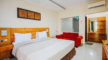 Una habitación de hotel con una cama grande, un sillón rojo, un aparador de madera y un aire acondicionado instalado en la pared.