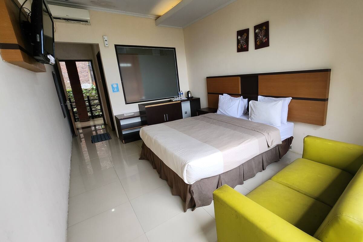 Quarto de hotel com cama, televisão, escrivaninha e poltrona amarela.