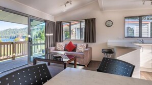 Een moderne woonkamer met een bank, bijzettafeltje en stoelen. Er is een schuifdeur naar een balkon met uitzicht op een meer en heuvels.