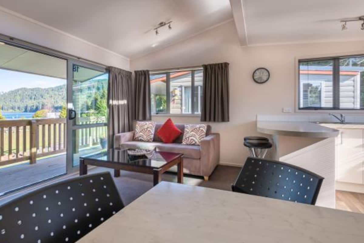 Un salon moderne avec un canapé, une table basse et des fauteuils. Une porte-fenêtre coulissante donne accès à un balcon d’où l’on peut admirer un lac et des collines.