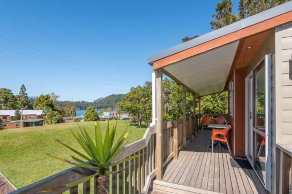 Une terrasse en bois dotée d’un espace abrité, d’une petite table et de chaises, et offrant une vue sur une zone herbeuse et des arbres.