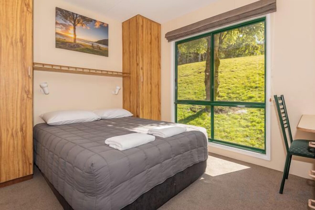 Une chambre à coucher avec un lit, une fenêtre, une chaise et un tableau accroché au mur.
