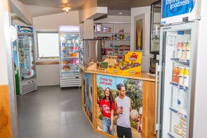 A food court with vending machines, a refrigerator stocked with beverages, and a poster advertising a beverage brand.