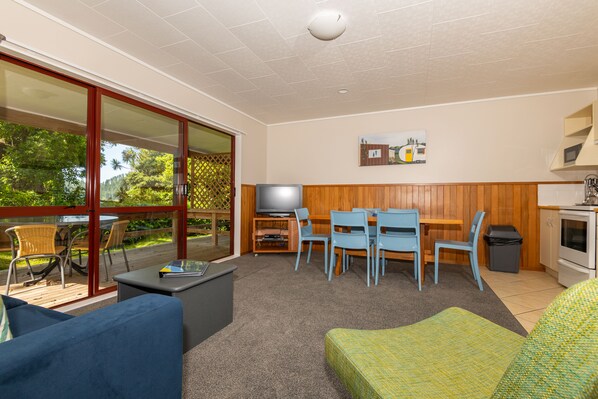 A living room with a TV, dining table, and chairs, a sofa, and a kitchen area with a stove.