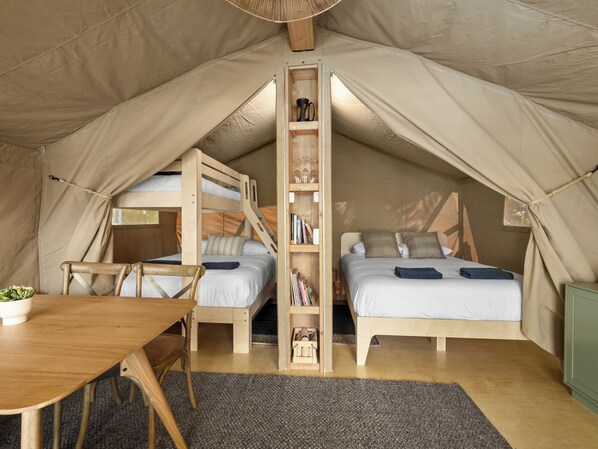A tent with two beds, a wooden table, and a bookshelf. - Rotorua Blue Lake Top 10 Holiday Park (Rotorua)