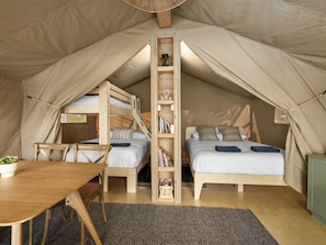 A tent with two beds, a wooden table, and a bookshelf.