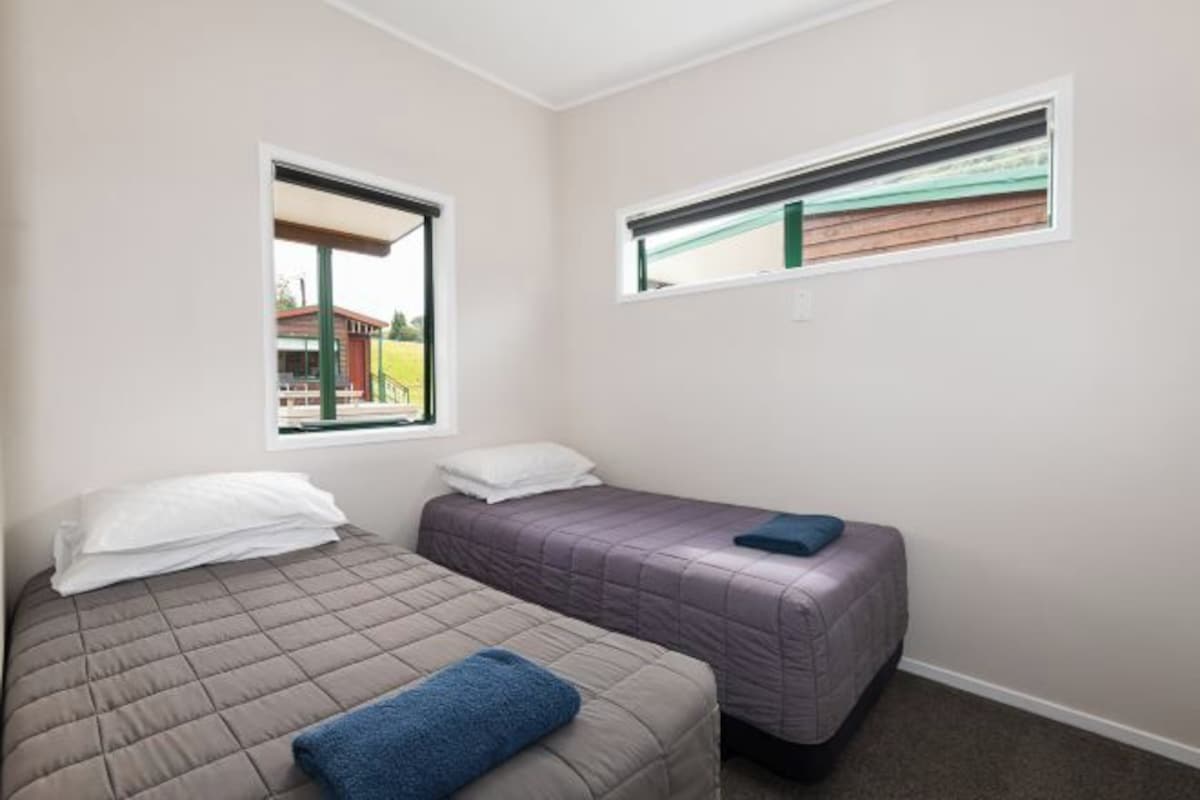 A bedroom with two beds, a window, and a view of a building outside.