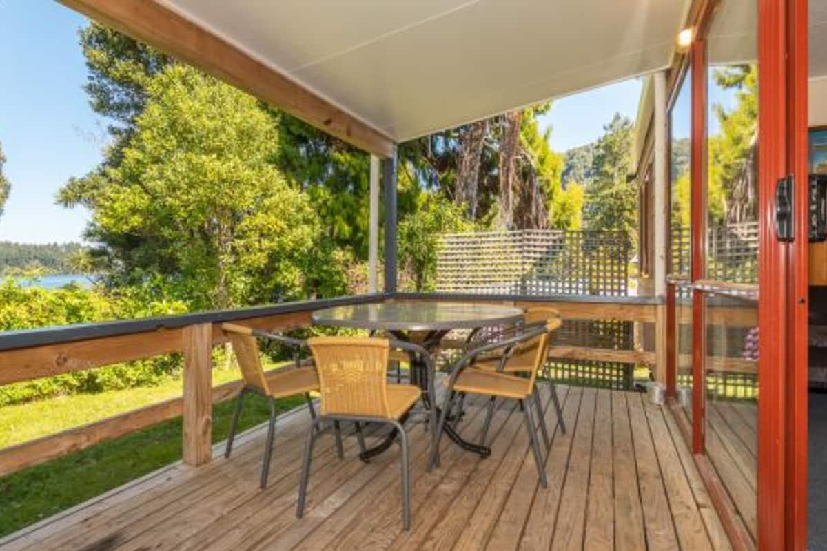 Une terrasse en bois avec une rambarde en verre, une table ronde et quatre chaises.