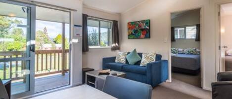 Una habitación moderna con un sofá azul, una mesa de comedor y un balcón con vistas a zonas verdes.