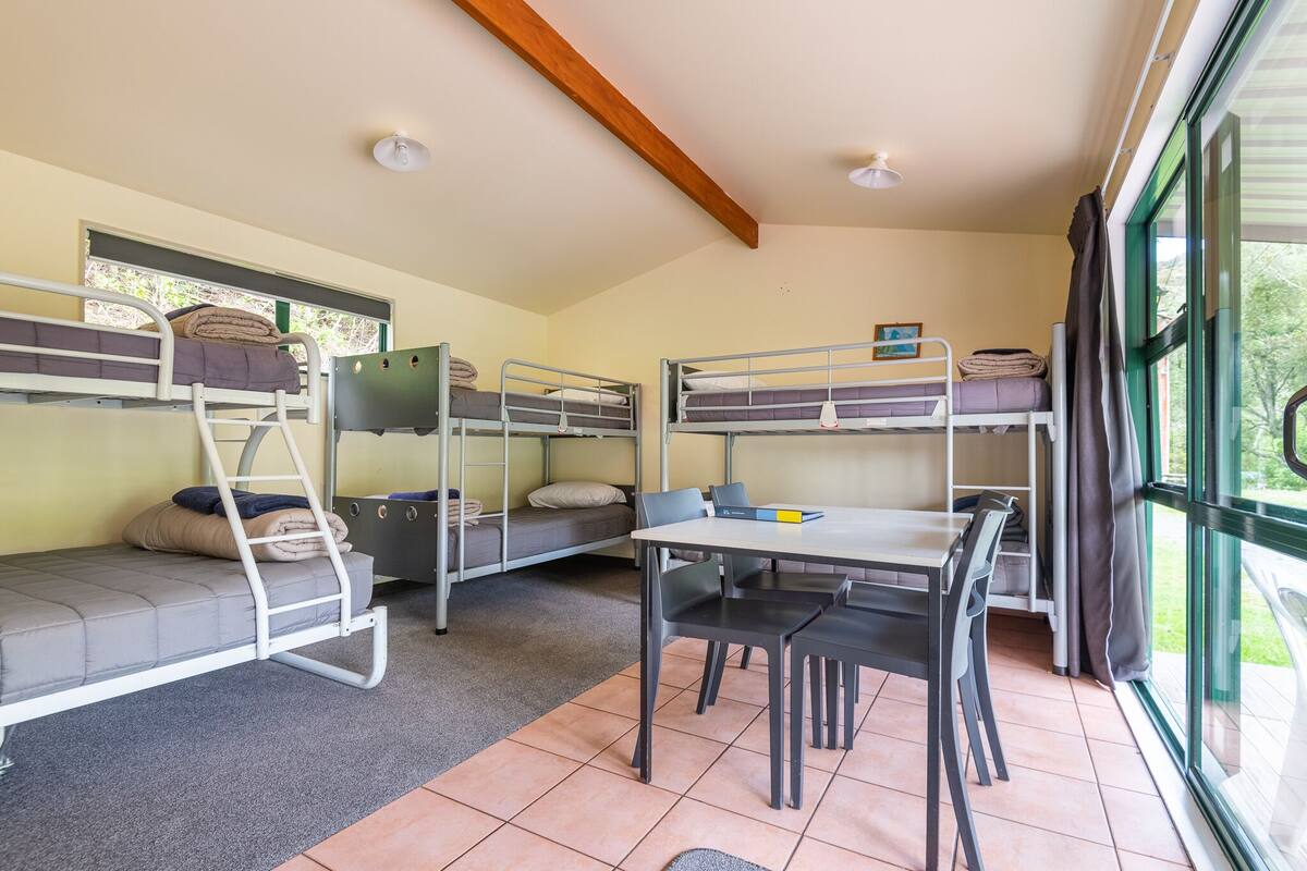 Une chambre de dortoir équipée de lits superposés, d’un bureau, de chaises et d’une fenêtre avec des rideaux.