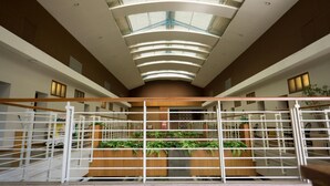 A modern interior with a central atrium, white railings, and green plants. - Hotel Asri Plaza Asia Tasikmalaya (Tasikmalaya)