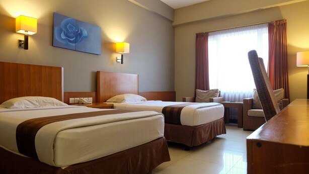 A hotel room with two beds, a wooden headboard, a desk, a chair, and a large window with curtains. - Hotel Asri Plaza Asia Tasikmalaya (Tasikmalaya)